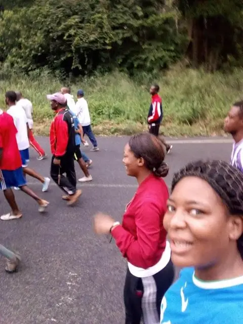 Deux jeunes femmes souriantes en tenue de sport pendant la marche, sur la route bordée de forêt.