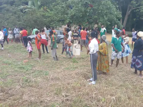 Des habitants de tous âges rassemblés sur un terrain herbeux du village.