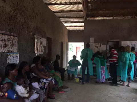 Le centre de santé plein de monde : soignants en blouse verte et familles venues consulter.